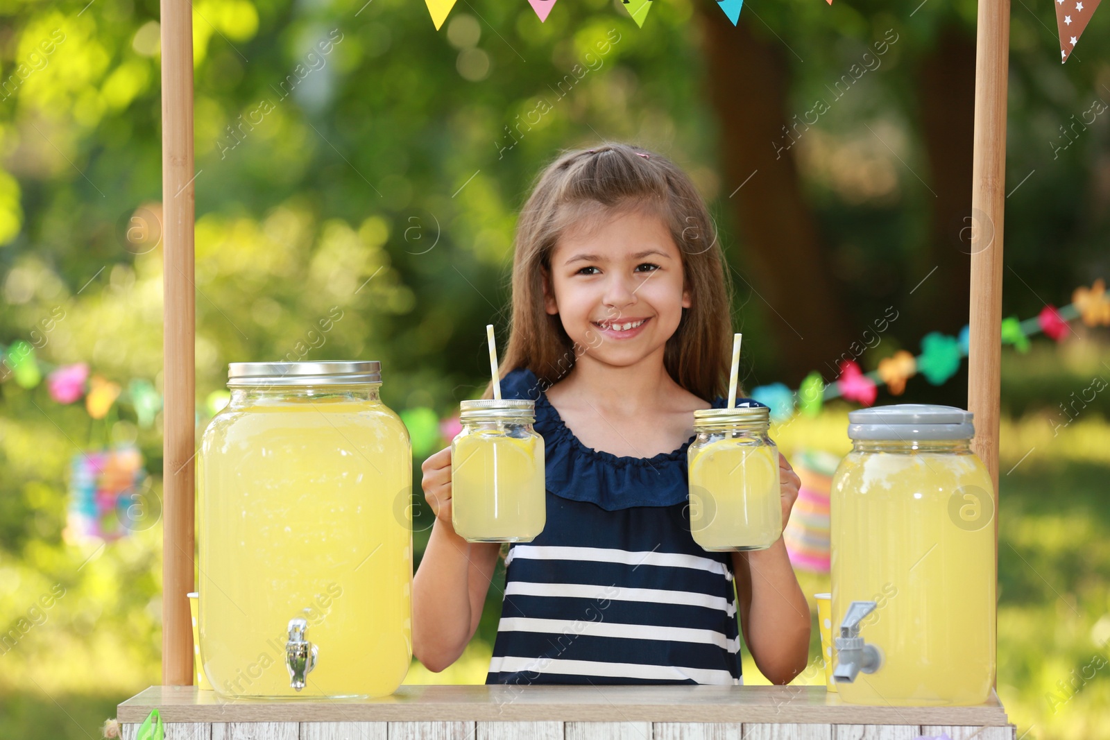 Photo of Cute little girl at lemonade stand in park. Summer refreshing natural drink