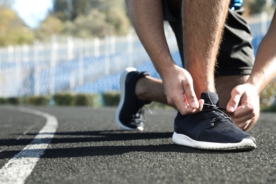 Photo of Sporty man tying shoelaces before running at stadium