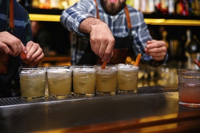 Photo of Bartenders preparing tasty cocktail at table in nightclub, closeup