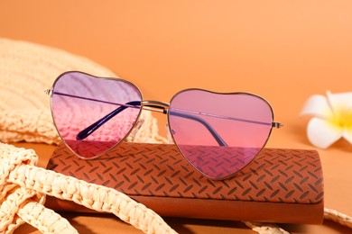 Photo of Stylish heart shaped sunglasses and brown leather case on pale orange background
