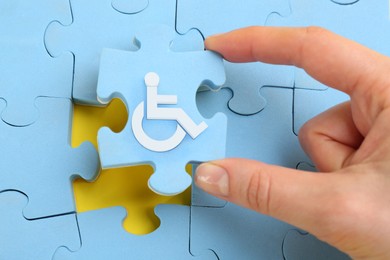 Image of Inclusion concept. Woman putting light blue puzzle with international symbol of access together, closeup