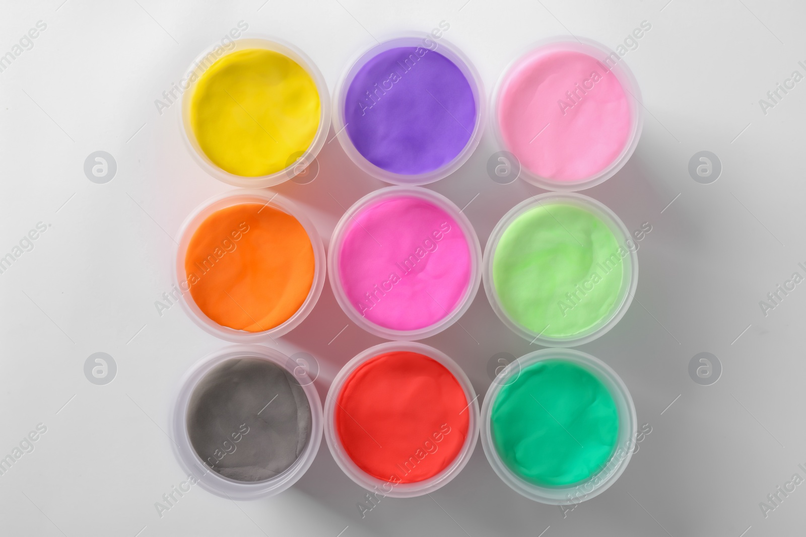 Photo of Plastic containers with different color play dough on white background, top view