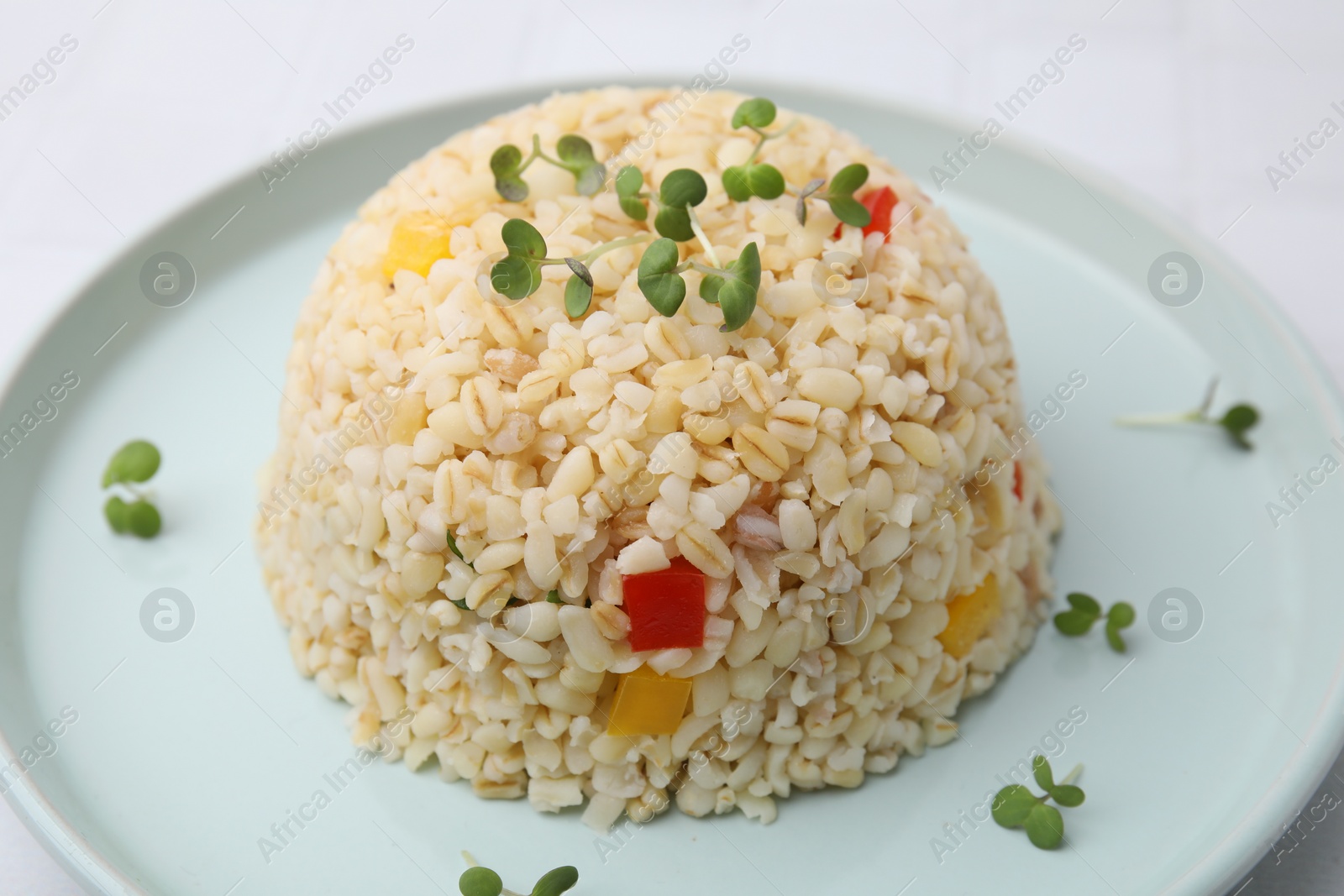 Photo of Delicious bulgur with vegetables and microgreens on table, closeup