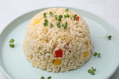 Delicious bulgur with vegetables and microgreens on table, closeup