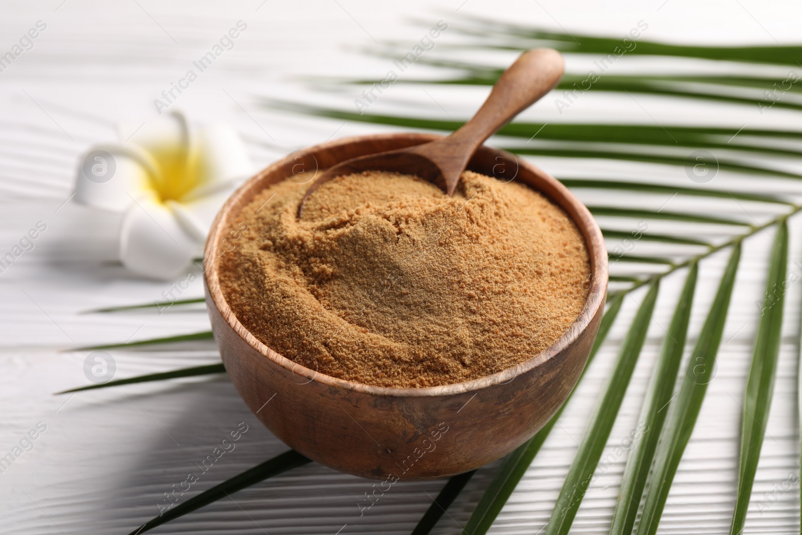 Photo of Coconut sugar and spoon in bowl on white wooden table, closeup