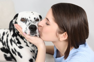 Photo of Beautiful woman kissing her adorable Dalmatian dog indoors, closeup. Lovely pet