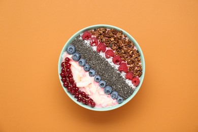 Photo of Tasty smoothie bowl with fresh berries and granola on orange background, top view
