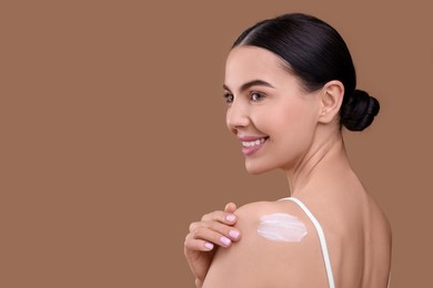 Photo of Beautiful woman with smear of body cream on her shoulder against light brown background, space for text