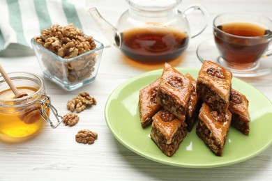 Photo of Delicious sweet baklava with walnuts, honey and hot tea on white wooden table