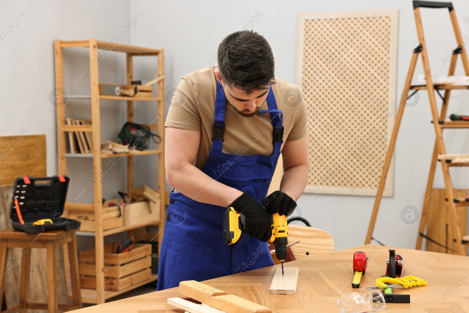 Photo of Young worker using electric drill at table in workshop