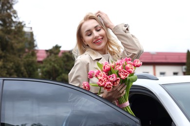 Happy young woman with beautiful bouquet near car outdoors