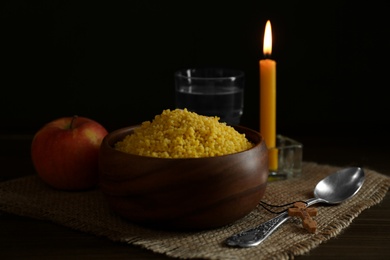 Photo of Millet, apple, water, burning candle and crucifix on wooden table. Great Lent season
