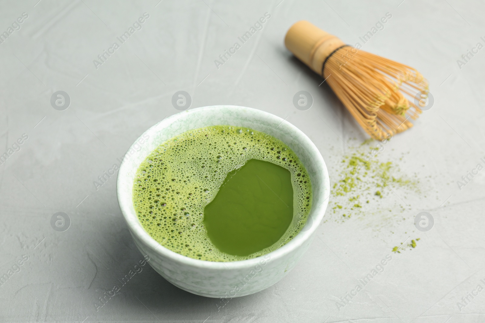 Photo of Bowl of fresh matcha tea and chasen on grey background