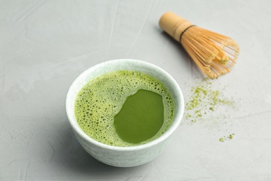 Photo of Bowl of fresh matcha tea and chasen on grey background