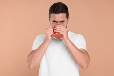 Photo of Man drinking from red mug on beige background