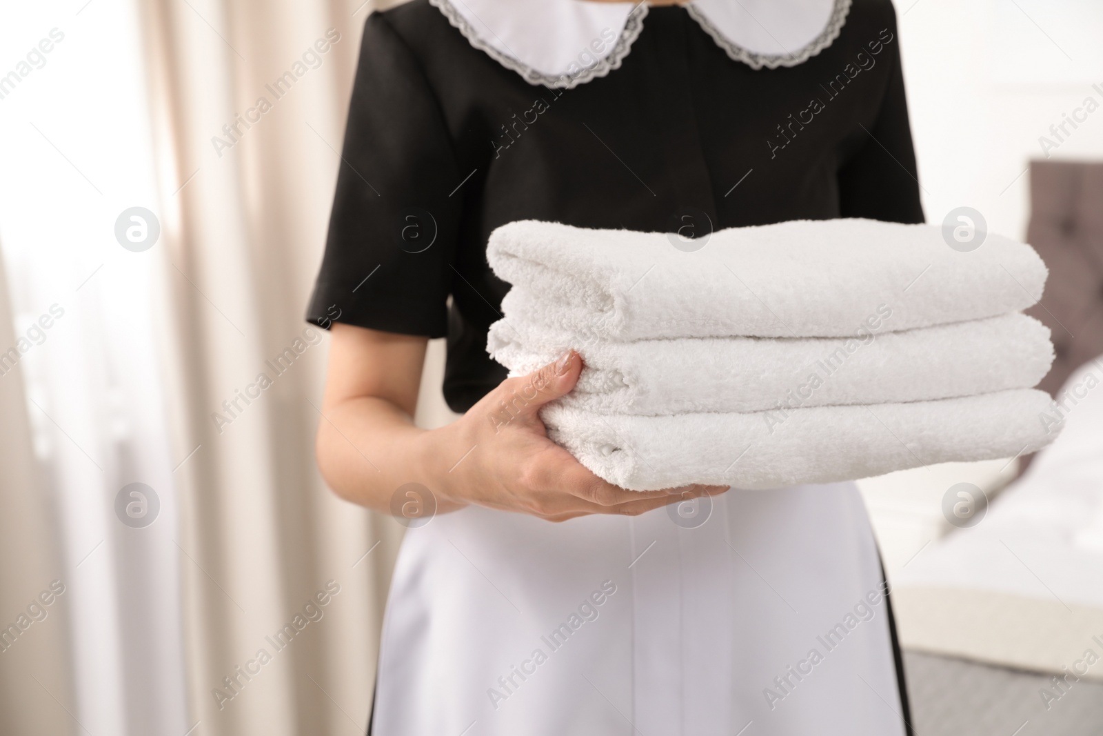Photo of Young maid holding stack of fresh towels in hotel room, closeup