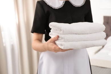 Young maid holding stack of fresh towels in hotel room, closeup