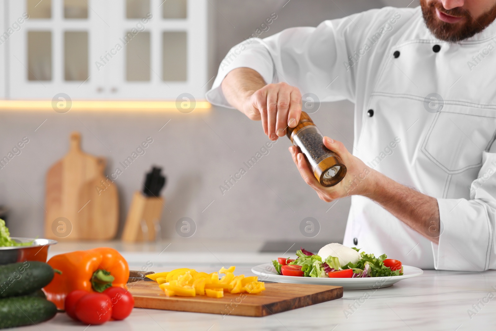 Photo of Professional chef adding pepper into delicious salad at marble table in kitchen, closeup. Space for text