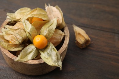 Photo of Ripe physalis fruits with calyxes in bowl on wooden table, closeup. Space for text