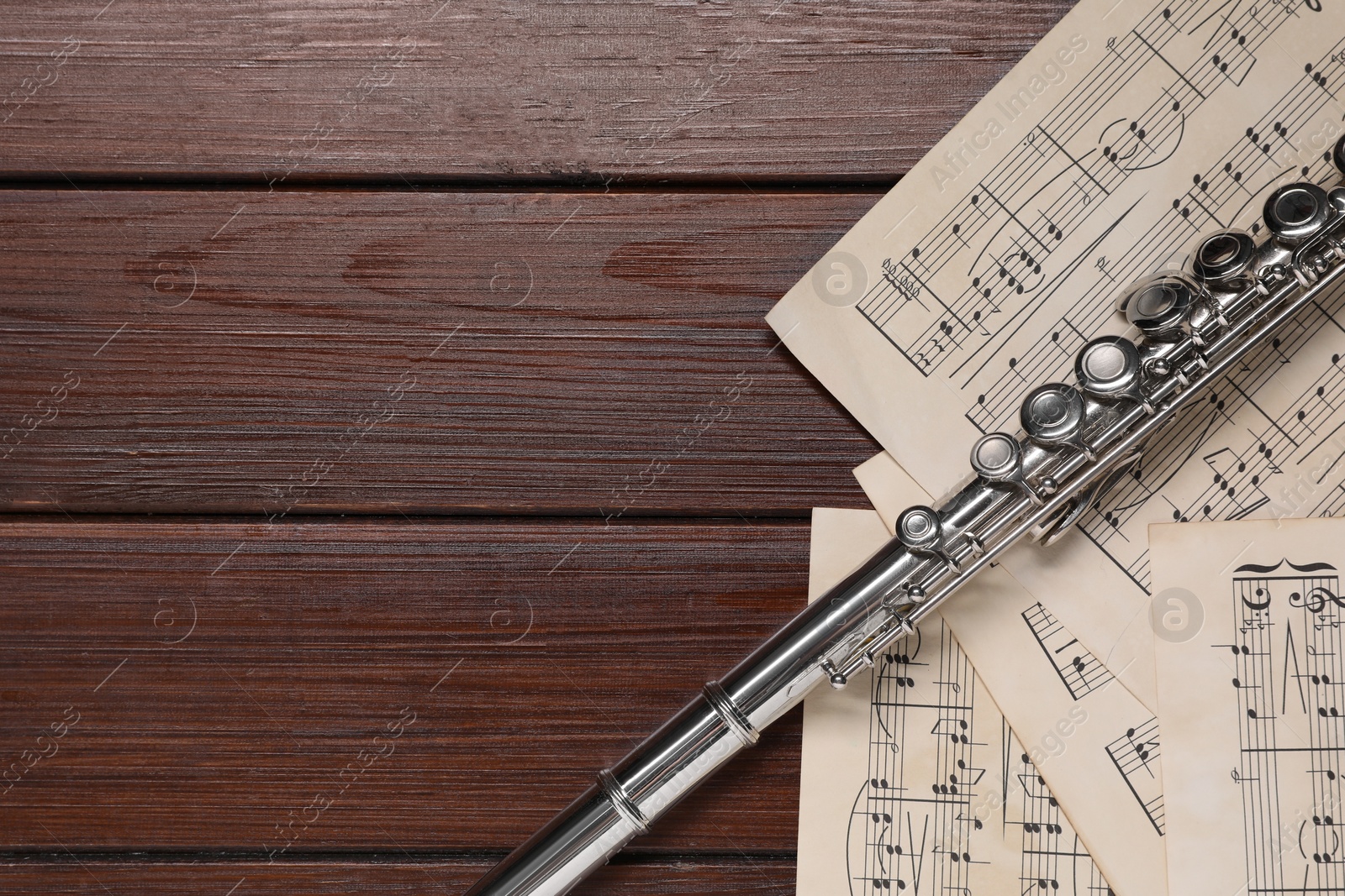 Photo of Sheets with musical notes and flute on wooden table, flat lay. Space for text