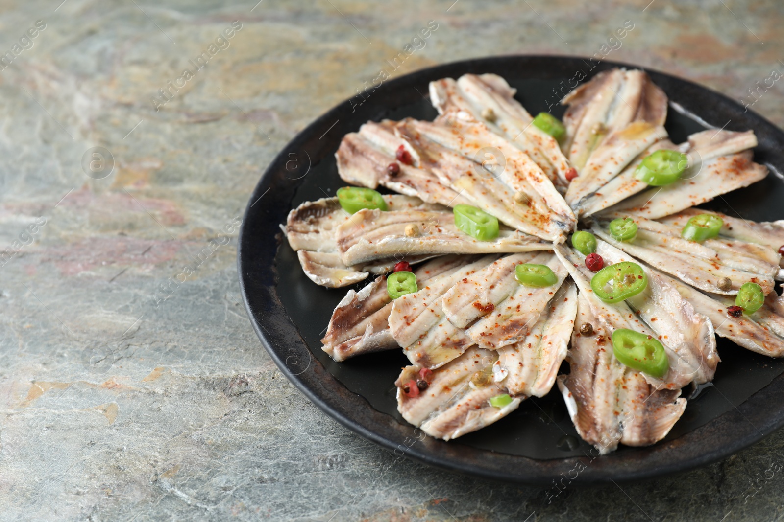 Photo of Tasty pickled anchovies with spices on textured table, closeup. Space for text