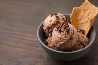 Tasty chocolate ice cream and piece of waffle cone in bowl on wooden table, closeup. Space for text