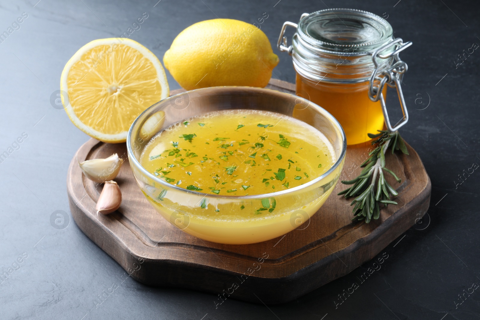 Photo of Bowl with lemon sauce and ingredients on dark table. Delicious salad dressing