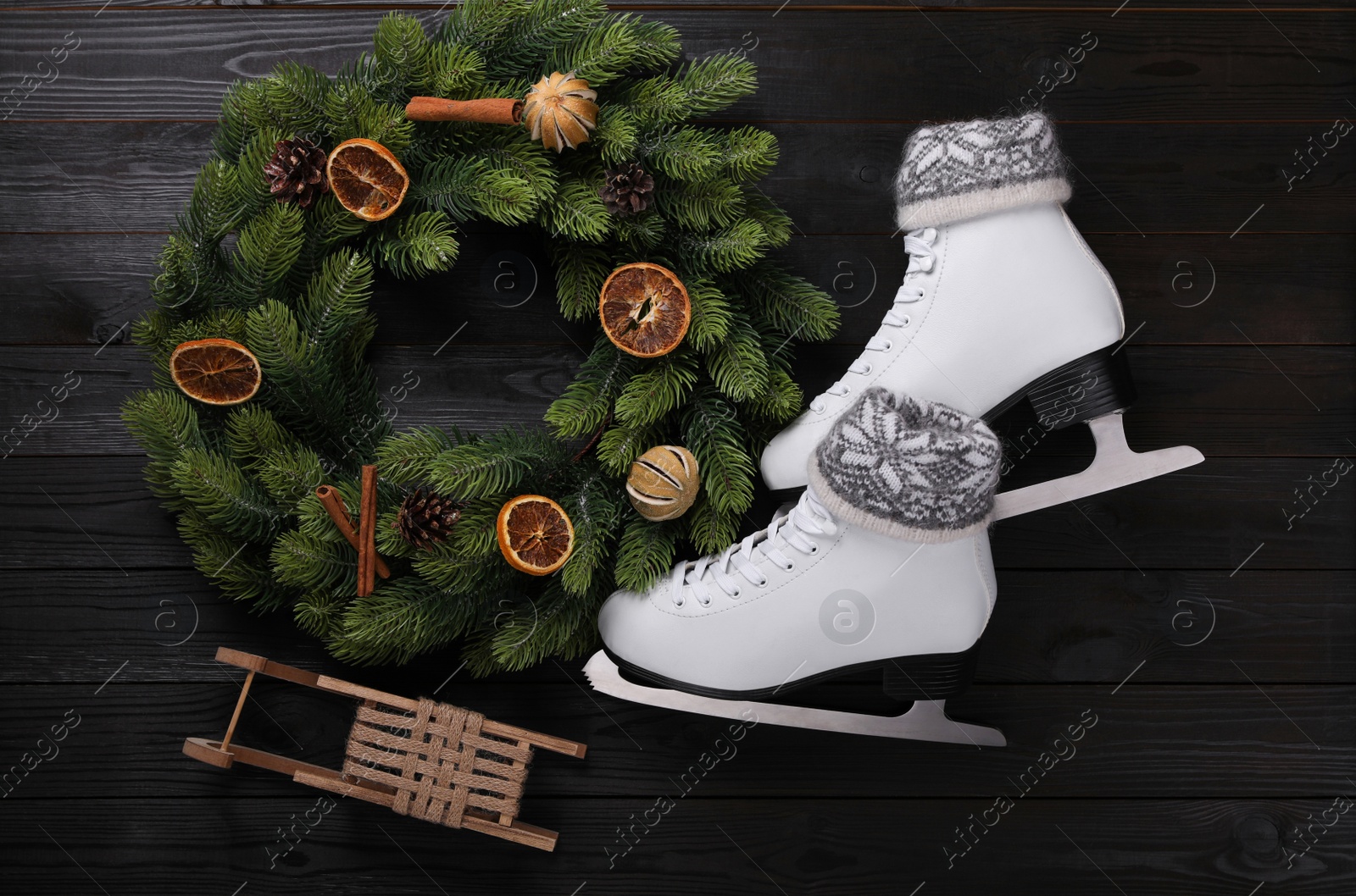 Photo of Pair of ice skates with Christmas decor on black wooden background, flat lay