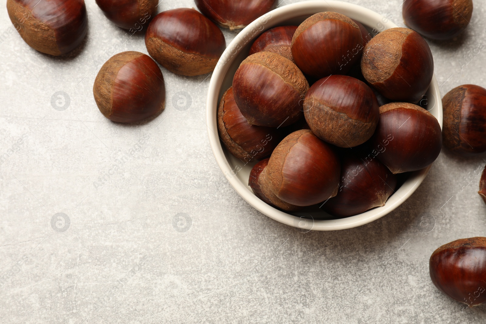 Photo of Bowl with roasted edible sweet chestnuts on light grey table, flat lay. Space for text