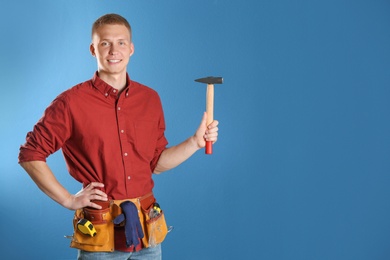 Handsome young working man with hammer against color background, space for text