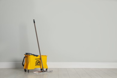 Photo of Mop and bucket on wooden floor near light grey wall, space for text. Cleaning service