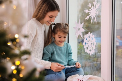 Photo of Happy mother and daughter near window decorated with paper snowflakes indoors