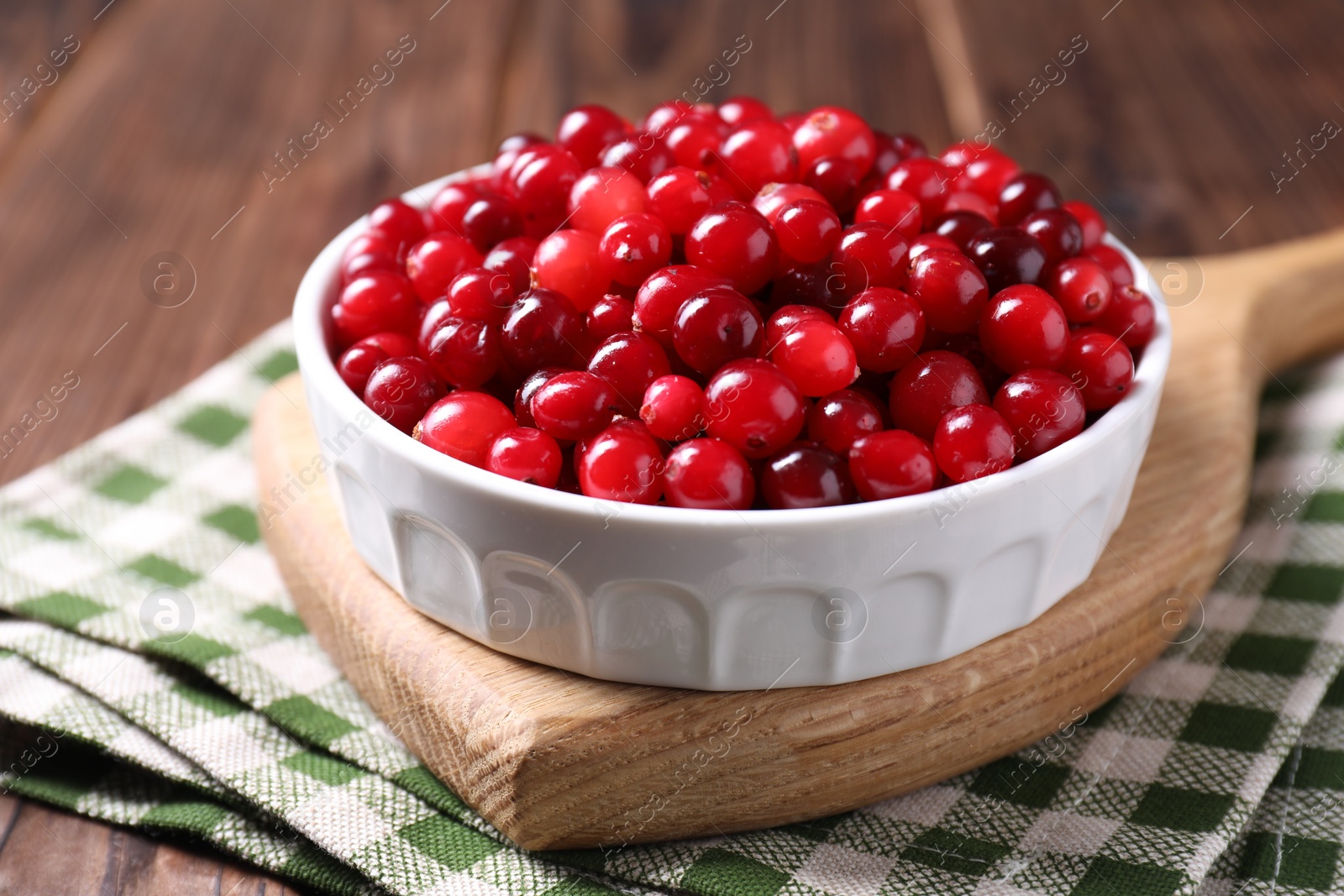 Photo of Fresh ripe cranberries in bowl on wooden table, closeup