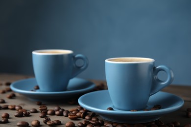 Photo of Cups of tasty espresso and scattered coffee beans on wooden table
