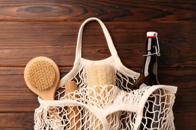 Fishnet bag with different items on wooden table, top view. Conscious consumption