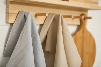 Photo of Different towels and wooden board hanging on rack in kitchen, closeup