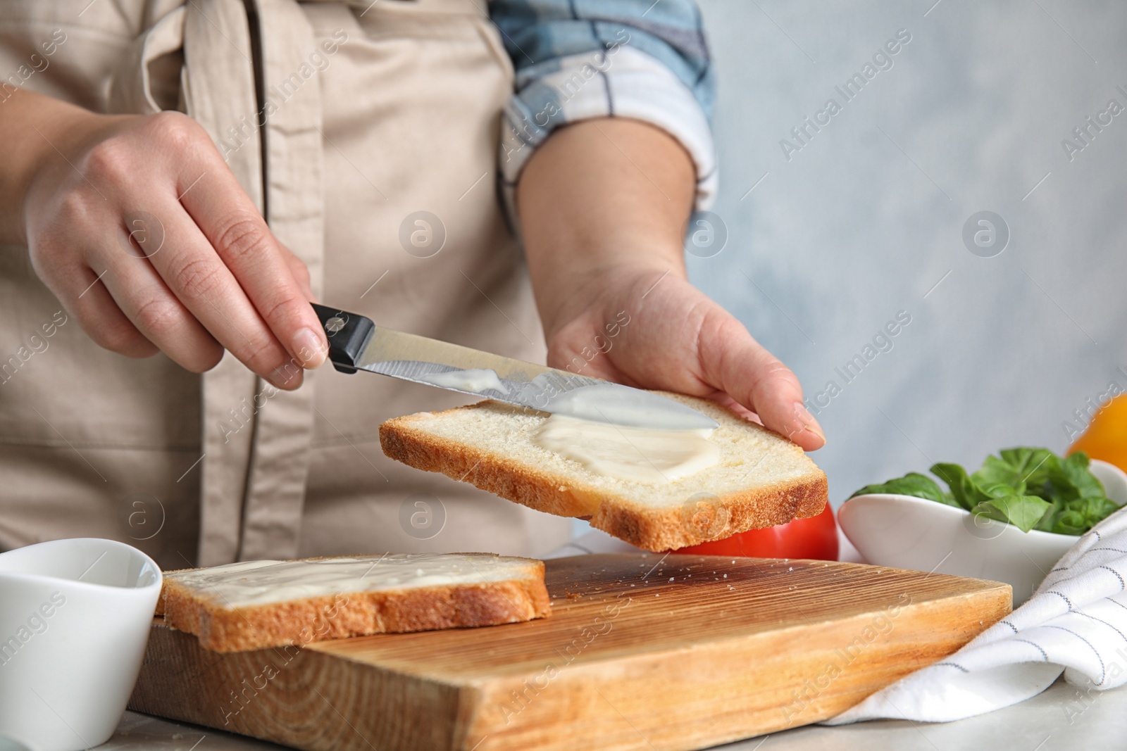 Photo of Woman spreading sauce on sandwich at light grey marble table, closeup