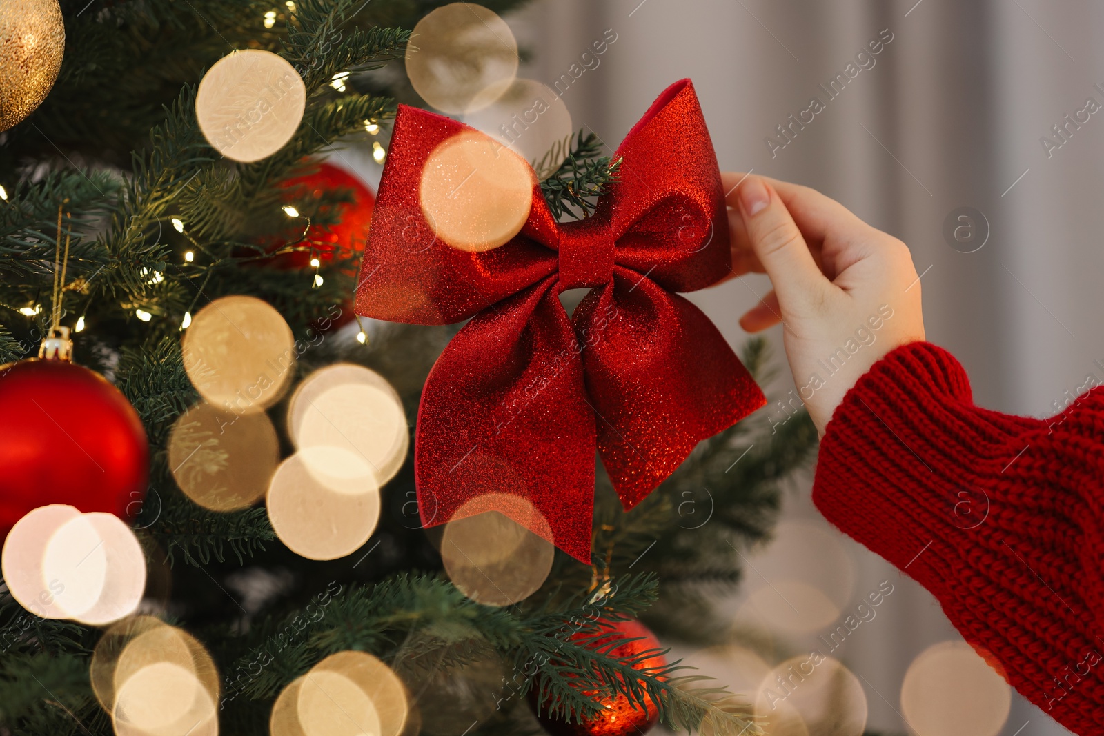 Photo of Woman decorating Christmas tree with red bow on light background, closeup