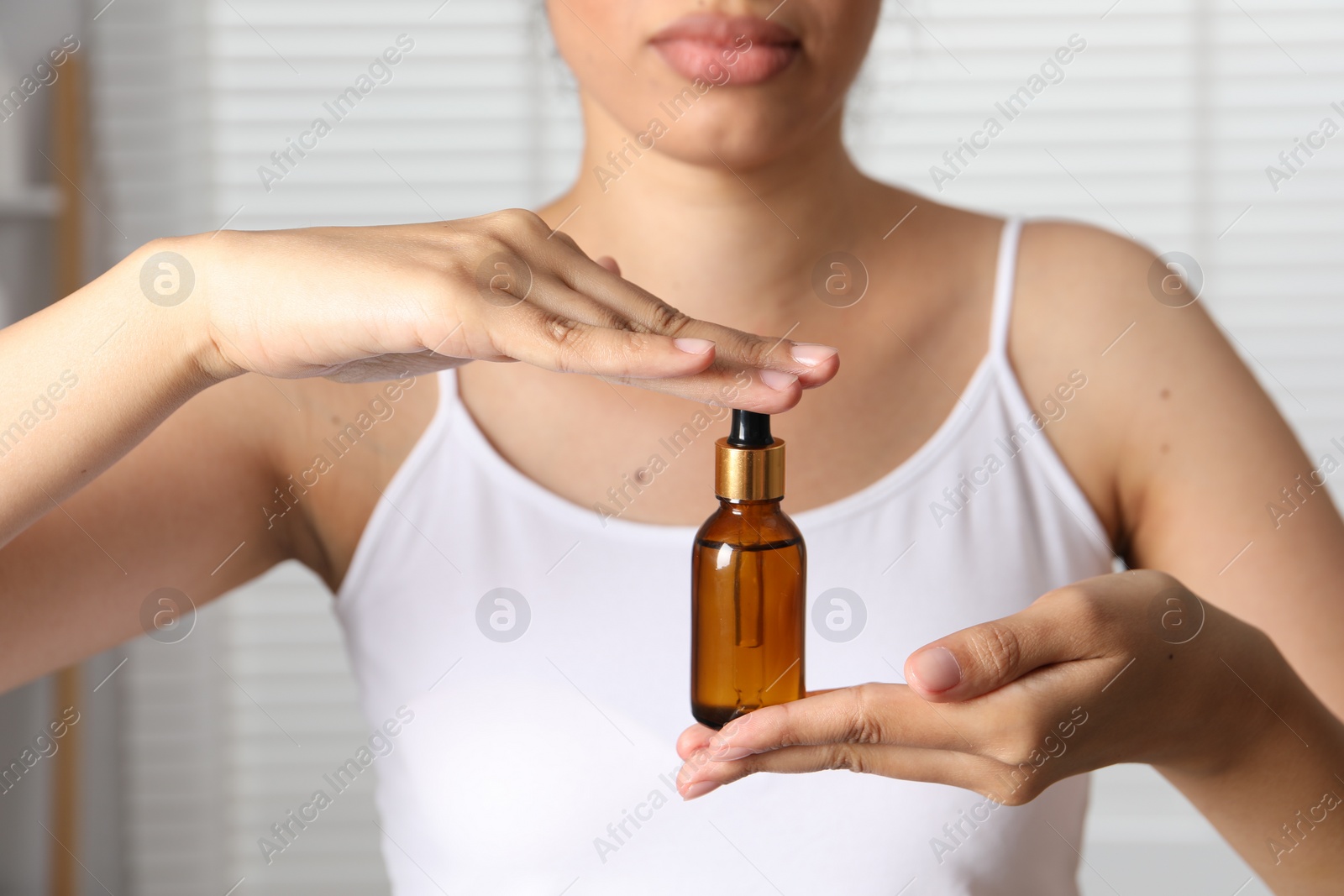 Photo of Woman with bottle of cosmetic serum on blurred background, closeup