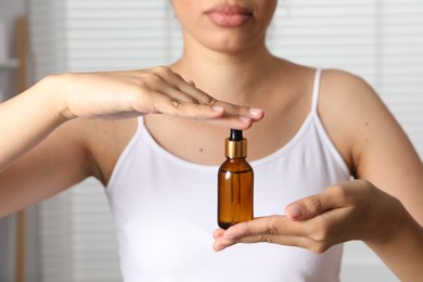 Woman with bottle of cosmetic serum on blurred background, closeup