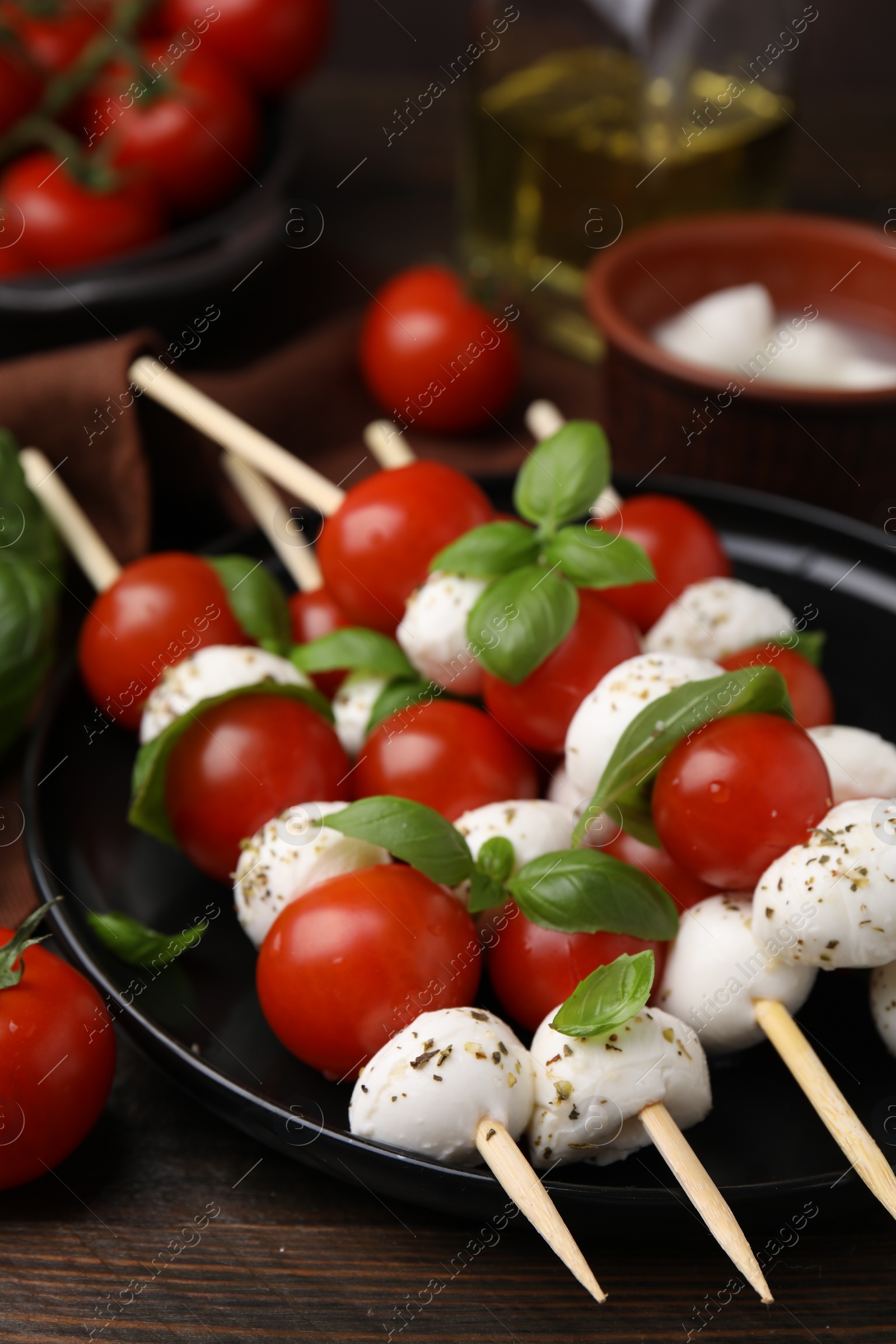 Photo of Delicious Caprese skewers with tomatoes, mozzarella balls, basil and spices on wooden table, closeup