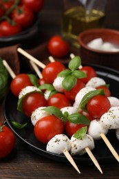 Photo of Delicious Caprese skewers with tomatoes, mozzarella balls, basil and spices on wooden table, closeup