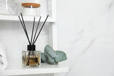 Photo of Aromatic reed air freshener on white wooden shelf in bathroom. Space for text