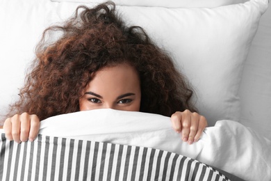 Photo of Young African-American woman lying under blanket, top view. Bedtime