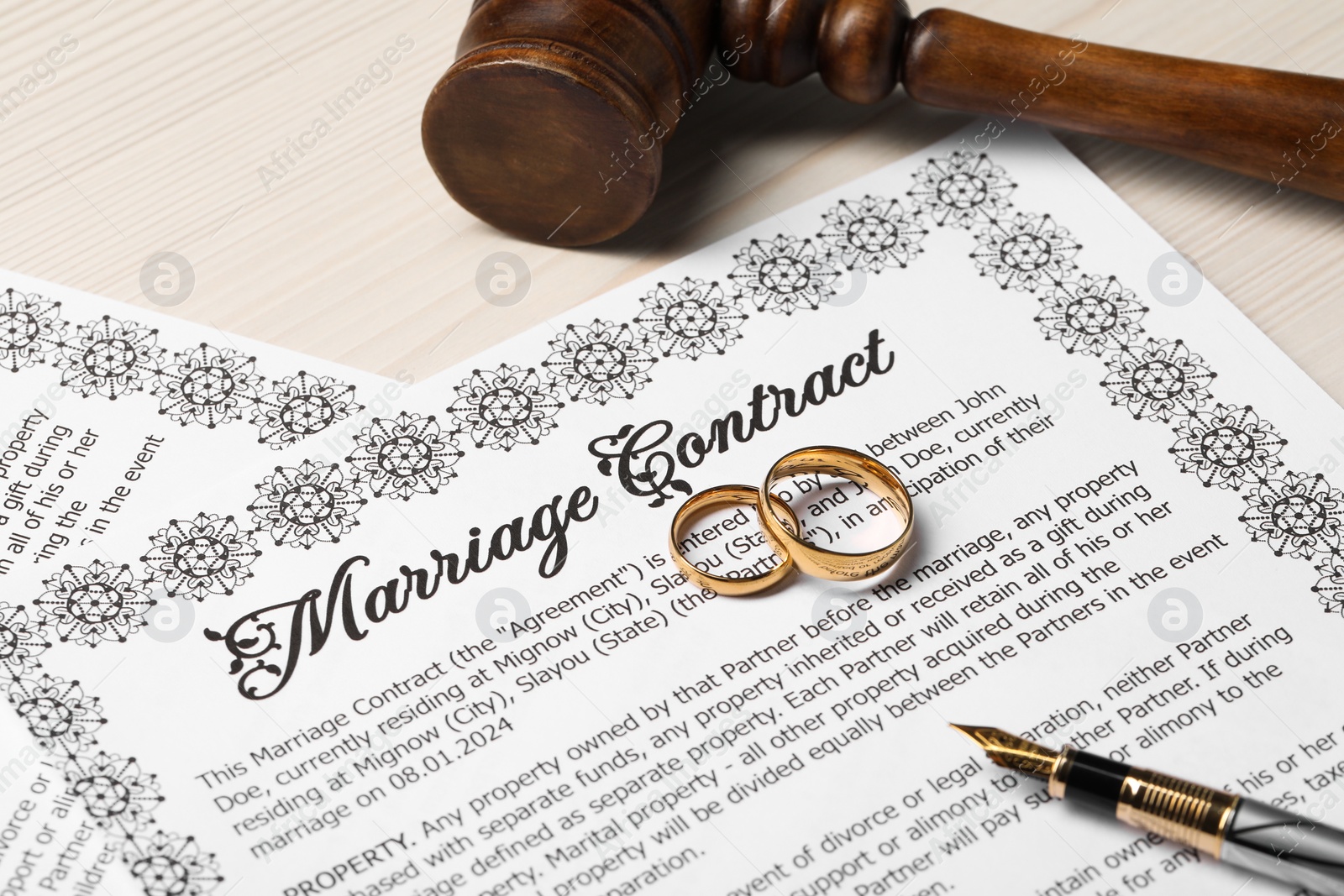Photo of Marriage contracts, gold rings, pen and gavel on light wooden table, closeup