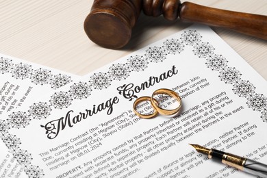 Marriage contracts, gold rings, pen and gavel on light wooden table, closeup