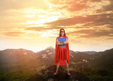 Image of Superhero, motivation and power. Woman in cape and mask on high top in mountains
