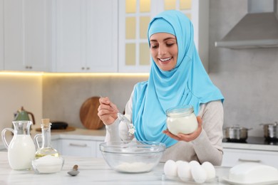 Photo of Muslim woman making dough at white table in kitchen. Space for text