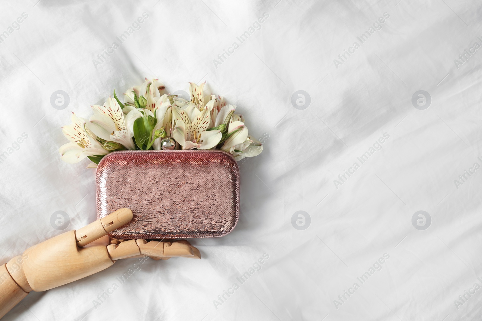 Photo of Stylish bag with spring flowers and wooden mannequin hand on crumpled sheet, flat lay. Space for text