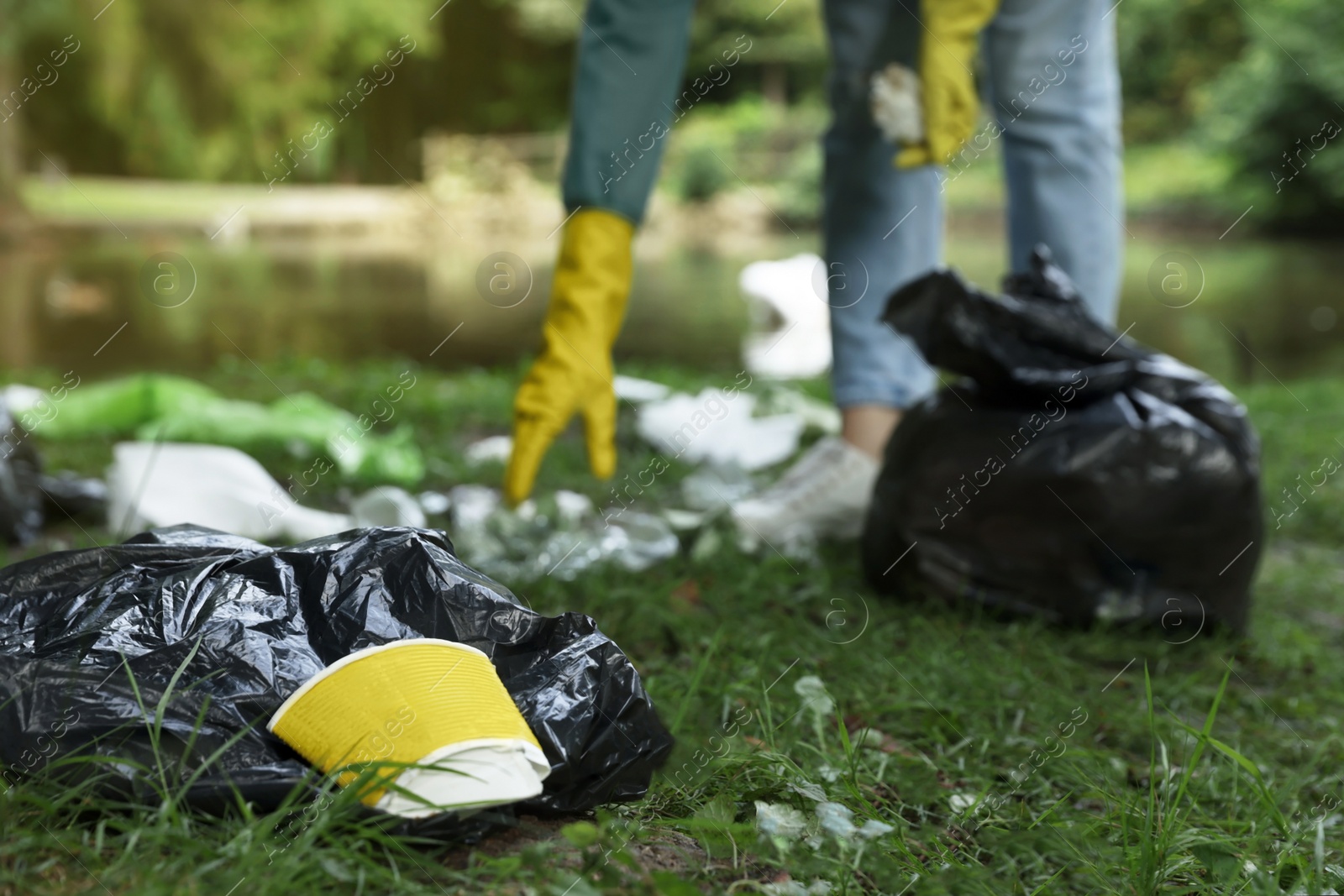 Photo of Woman collecting garbage in park, focus on paper cup. Space for text